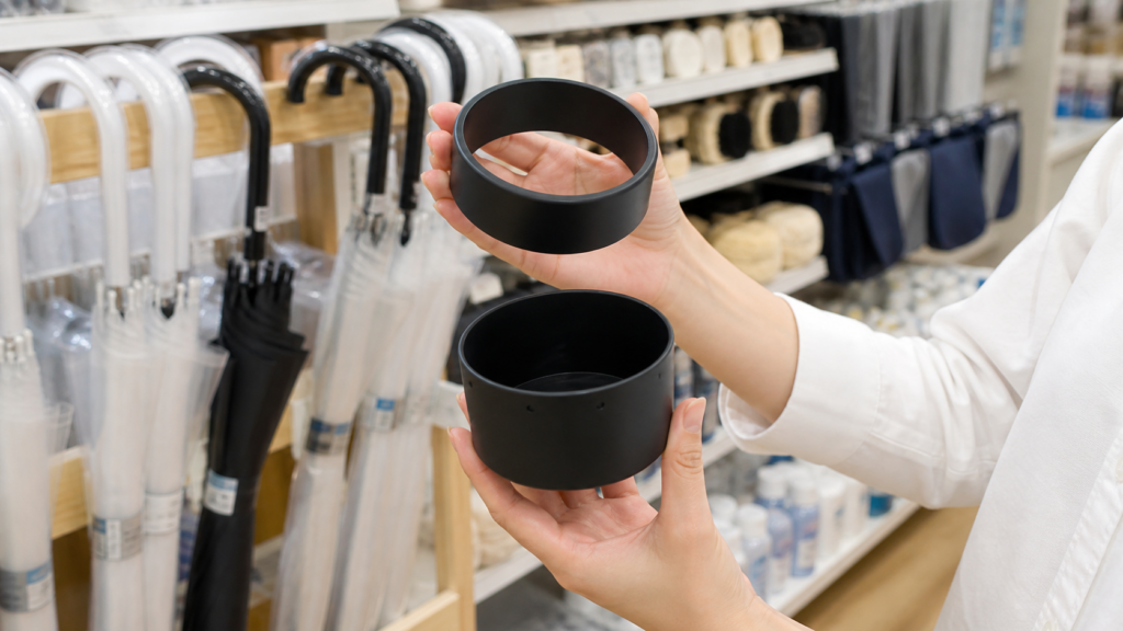 100円ショップの傘・レイングッズ売り場で黒いマグネット式傘ホルダーを探すイメージ